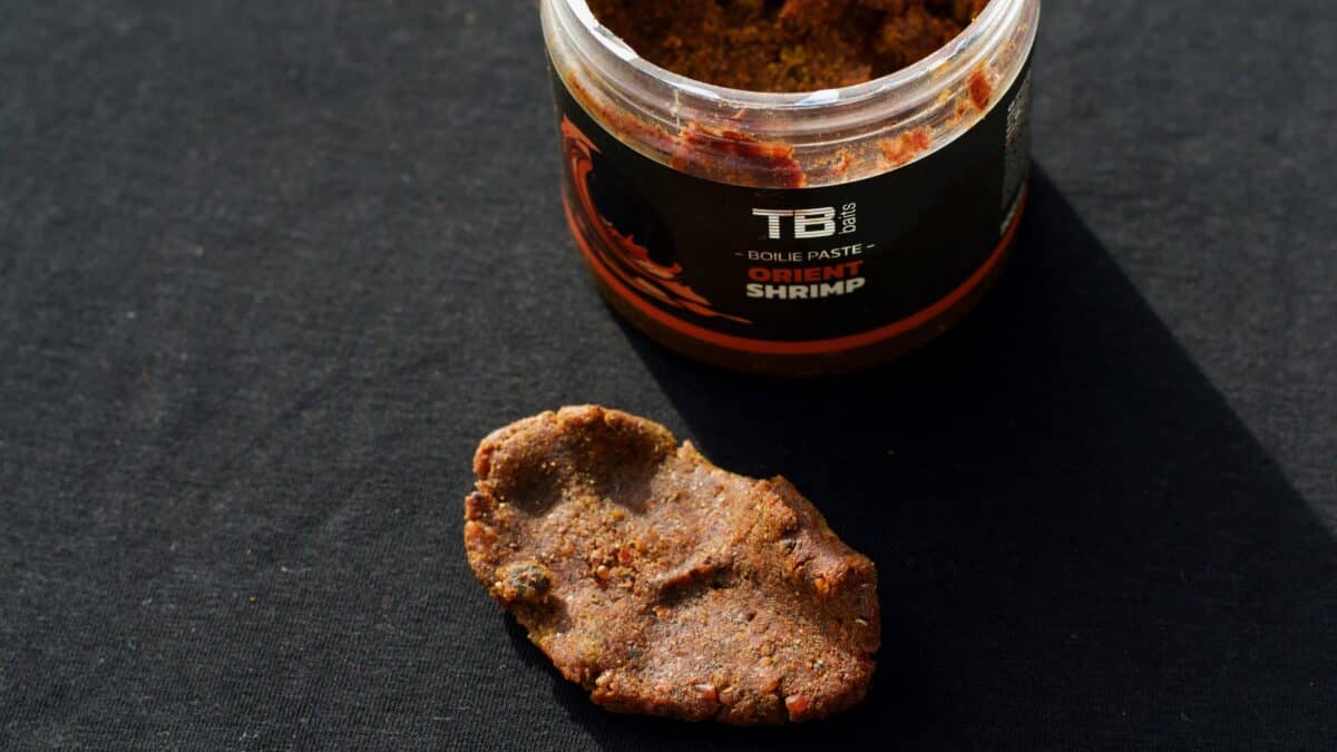 Open jar of TB Baits Oriental Shrimp boilie paste with a chunky bait piece on a dark surface