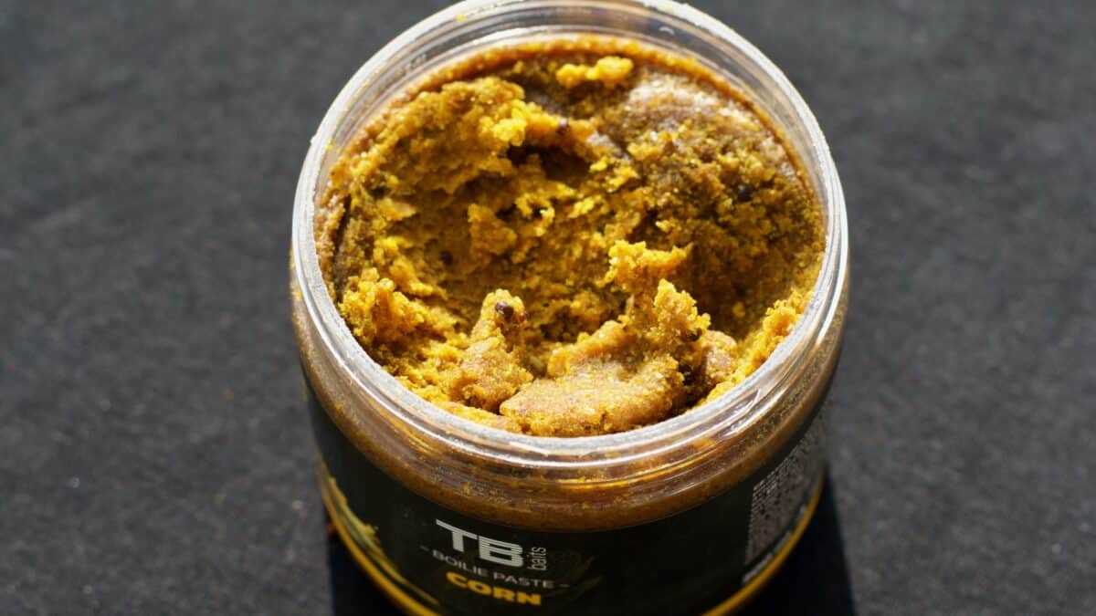 Top view of a glass jar containing chunky brown paste, likely peanut butter, on a dark surface.