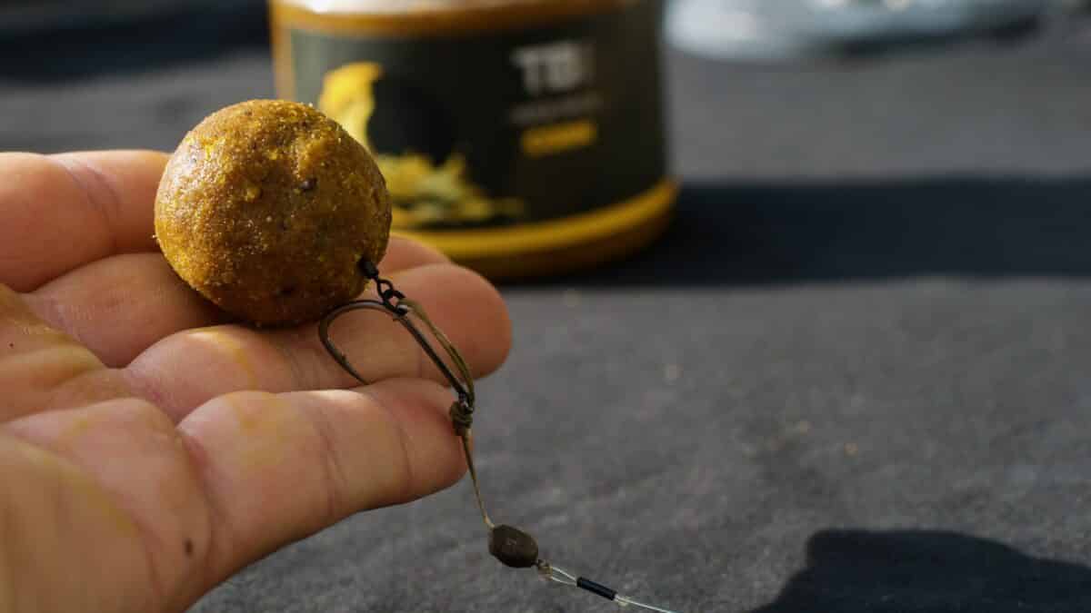 Close-up of a brown round bead on a fishing lure being held between fingertips, with fishing line and a small swivel visible.