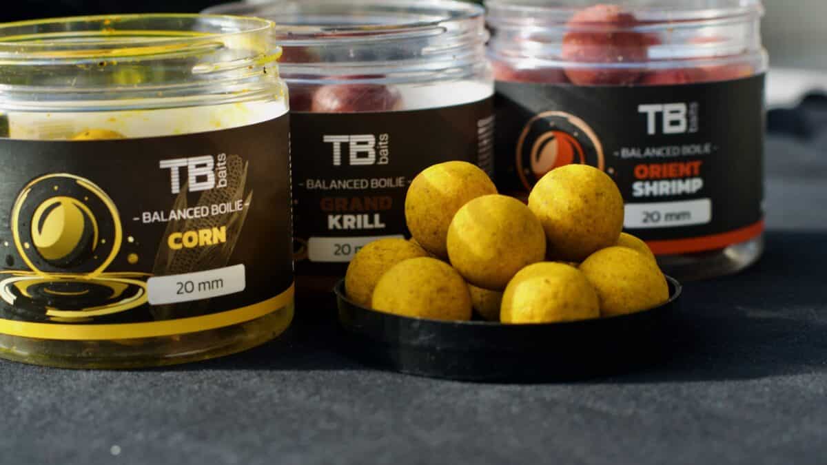 Three TB Baits jars of balanced boilies labeled Corn, Grand Krill, and Orient Shrimp with yellow boilies in front.