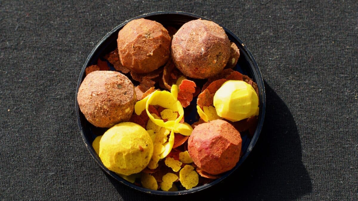 Round, blue container holding orange and yellow bath bombs with broken fragments on a dark fabric surface.