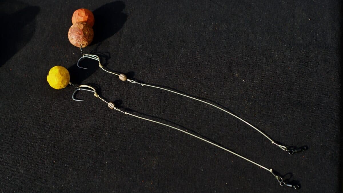Close-up of a beaded fishing lure rig with yellow and orange beads and metal hooks on a dark fabric background.