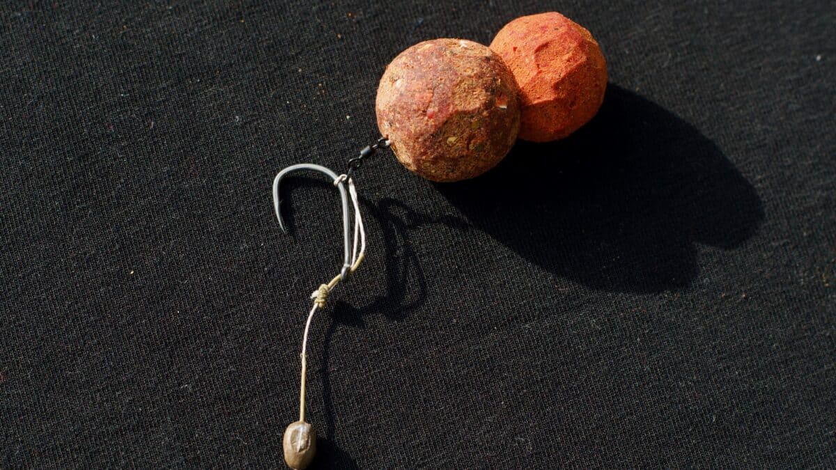 Two rough, textured beads (one brown, one orange) tied to a metal hook on dark fabric.1